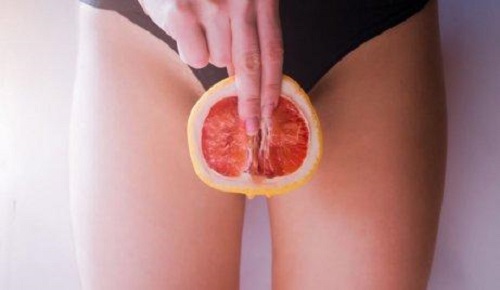 Femeie care ține un grepfrut în zona genitală