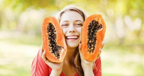 Femeie pozând cu un papaya tăiat în două