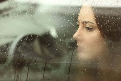 Femeie privind printr-un geam udat de ploaie
