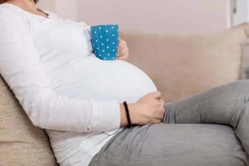 Femeie gravidă cu cana de ceai pe burtă