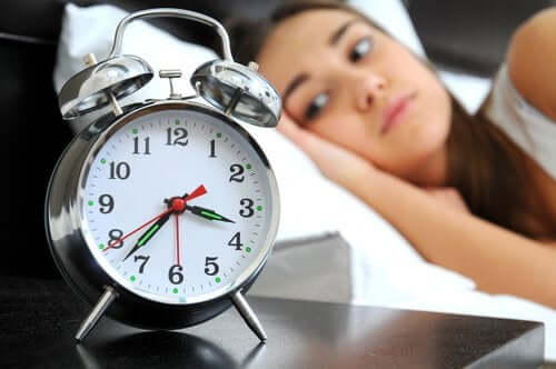 Femeie cu insomnie privind ceasul de pe noptieră