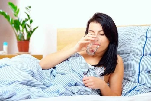 Femeie care bea apă stând în pat