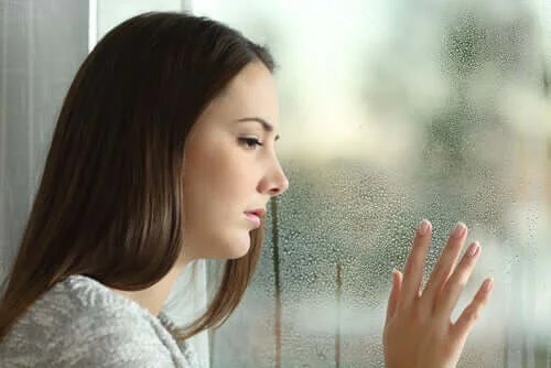 Femeie tristă care se uită pe geam