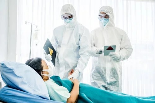 Bolnav pe patul de spital vizitat de medici în PPE