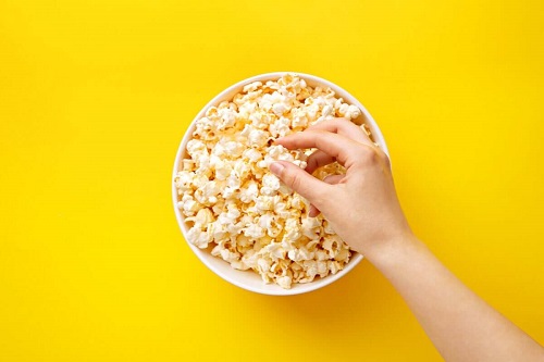 Mână luând popcorn dintr-un castron