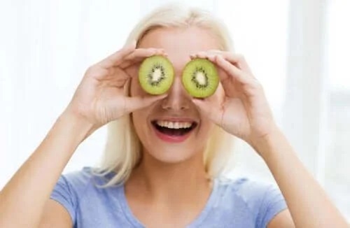 Femeie care ține felii de kiwi pe ochi