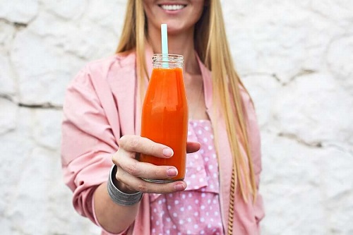 Fată care ține o sticlă cu suc de morcovi