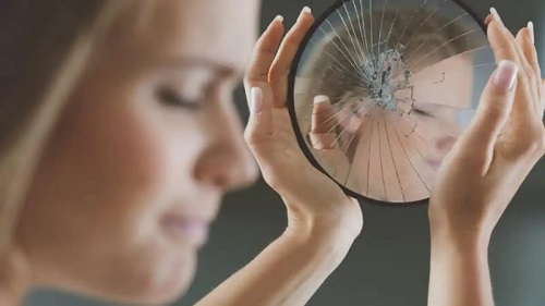 Femeie care ține o oglindă spartă