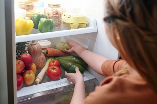 Femeie care pune legume în frigider