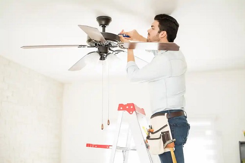 Bărbat care se ocupă cu pași pentru curățarea ventilatoarelor de tavan