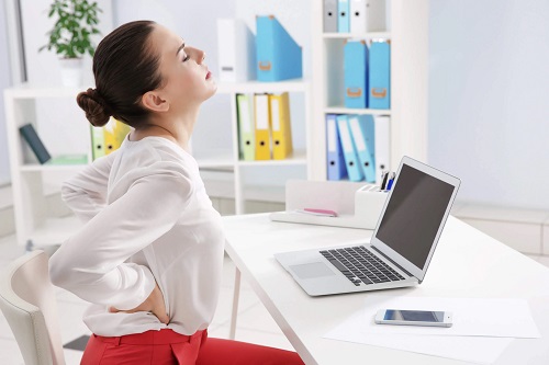 Femeie cu dureri de spate stând la birou