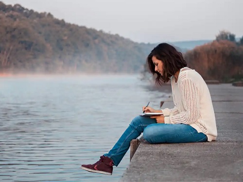 Femeie care scrie lângă un lac